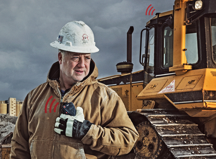 Aina promotional image showing man wearing white hard hat and work jacket with construction digger in the background.