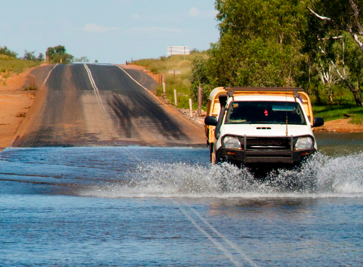 Australian ute driving through flooded waters on an empty road.