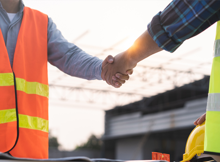 Close up photo of two people shaking hands on a construction site.