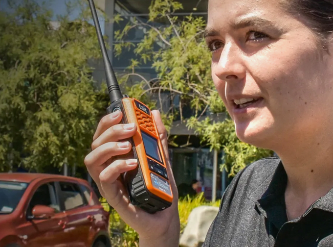 Lady holds an orange Tait TP3 DMR portable as she stands in a car park.