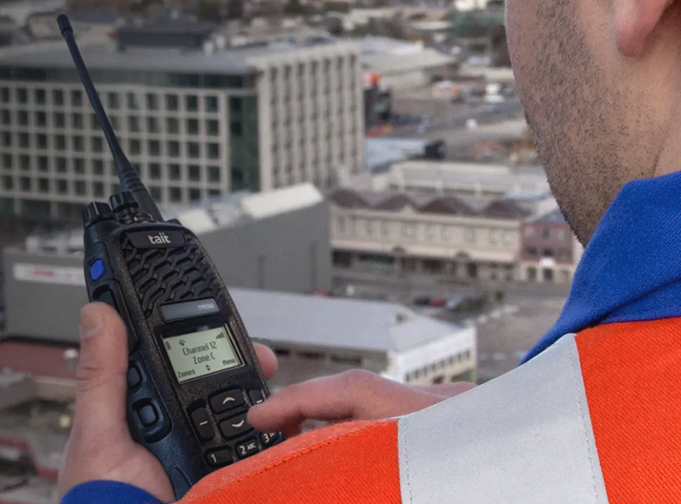 Utility worker holding a black Tait DMR TP9300 portable while up high in a building.