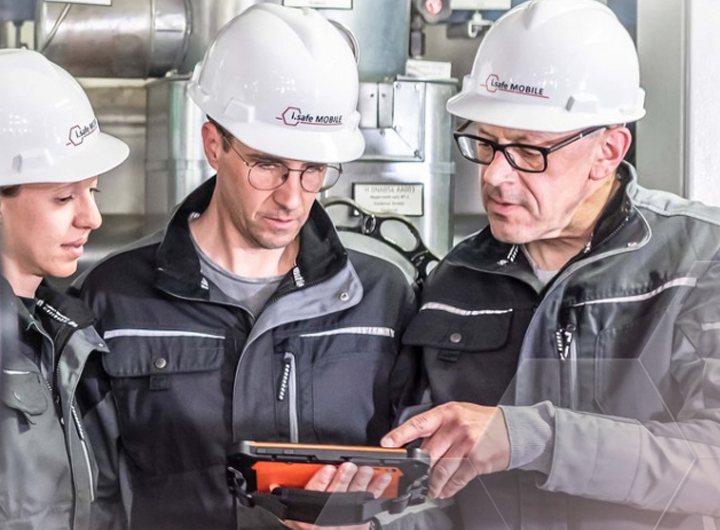 safe.MOBILE hero image of three people in a manufacturing plant wearing hard hats and looking at an i.safe MOBILE tablet device
