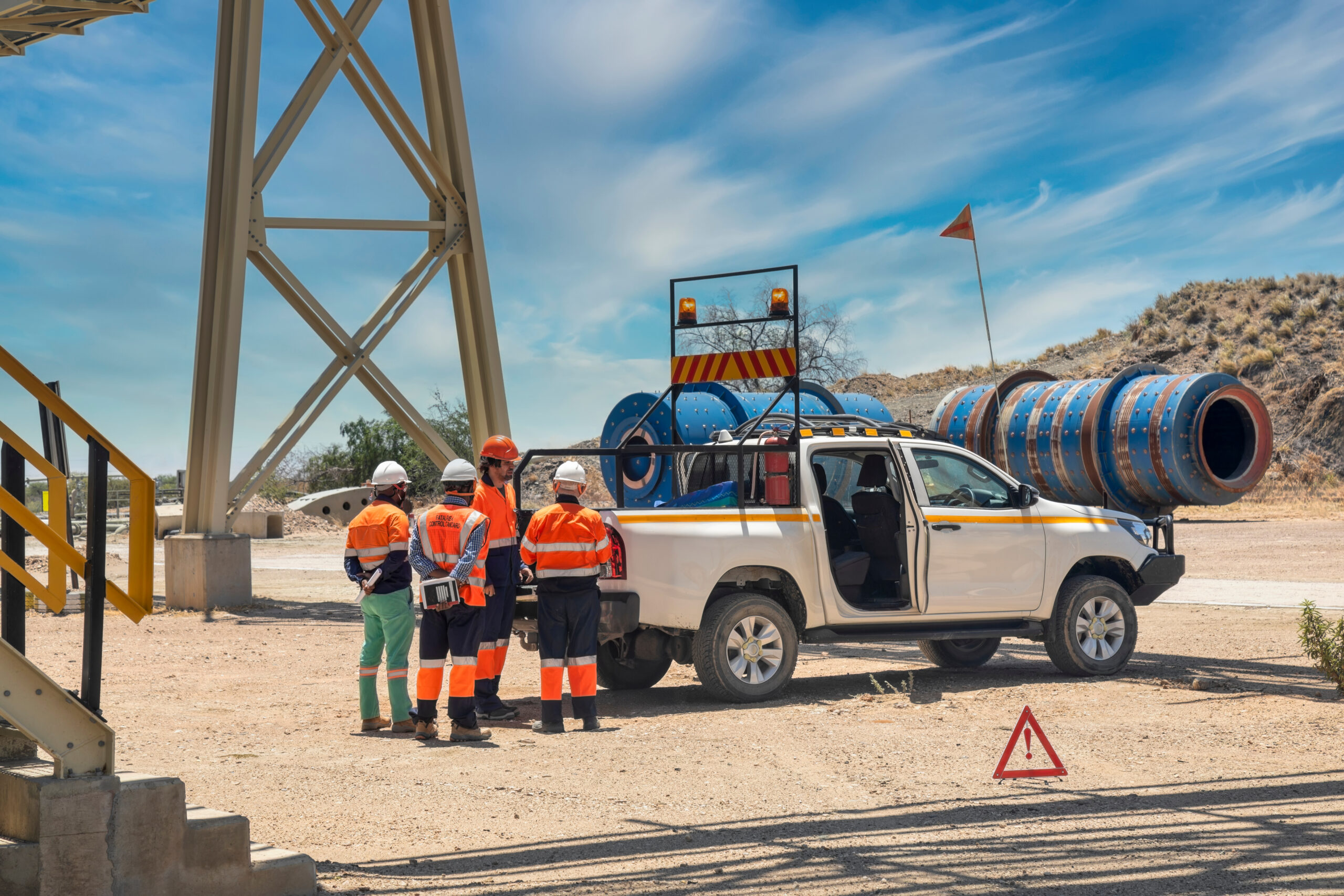 Managers on a diamond mine site in Australia in discussion next to a white ute on a dirt road under a bridge.